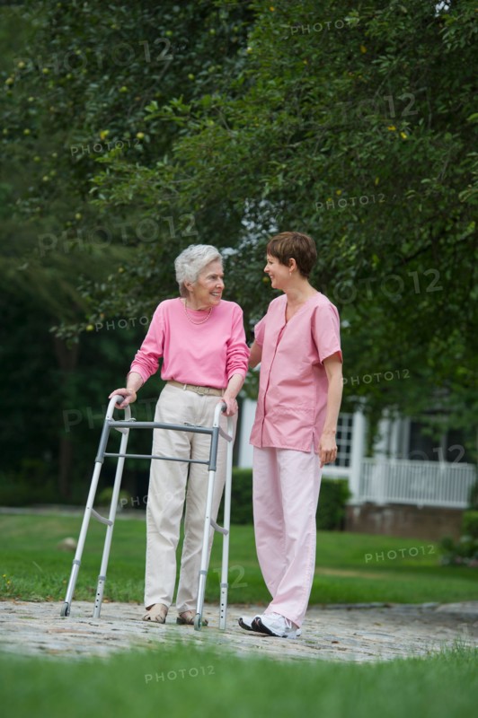 Senior woman walking with walker with help of nursing assistant.