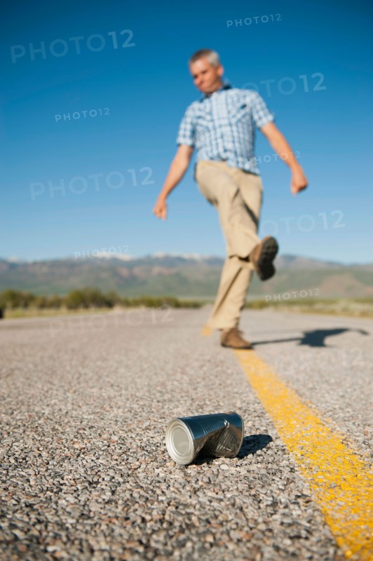 Man kicking tin can on otherwise empty road.