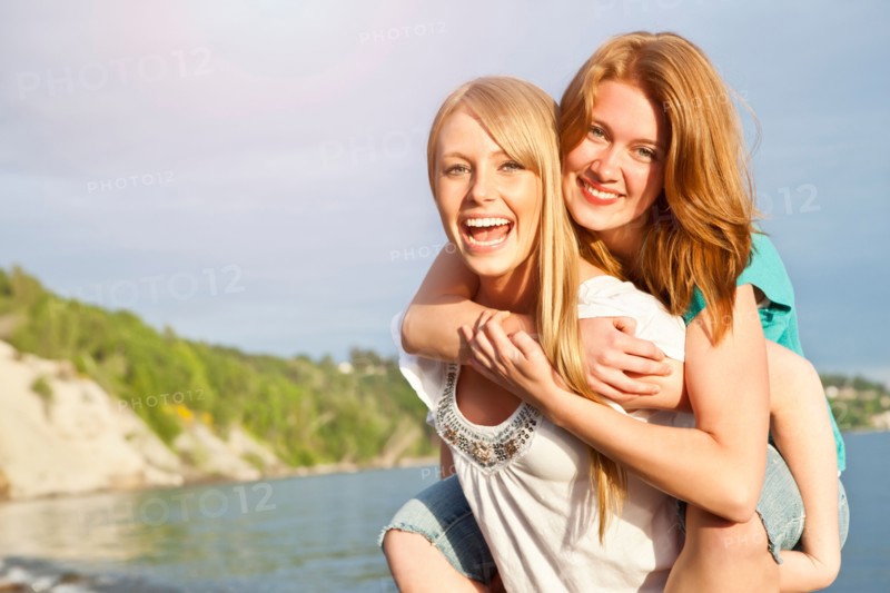 Portrait of two young women piggy-backing on beach. Photo : Take A Pix Media