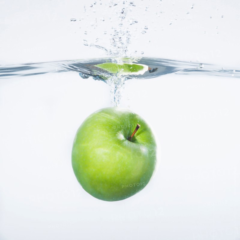Green apple splashing into water, studio shot. Photo : Daniel Grill