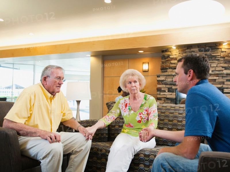 Senior people holding hands in hospital talking to doctor. Photo: Erik Isakson