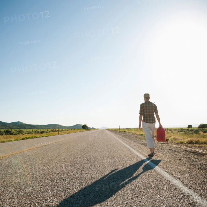 Mid adult woman carrying empty canister along empty road. Photo: Erik Isakson