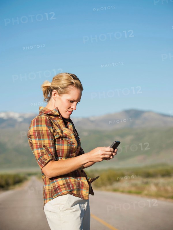 USA, Utah, Kanosh, Mid adult woman calling emergency services on empty desert road. Photo: Erik Isakson