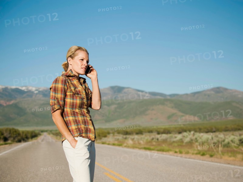USA, Utah, Kanosh, Mid adult woman calling emergency services on empty desert road. Photo: Erik Isakson