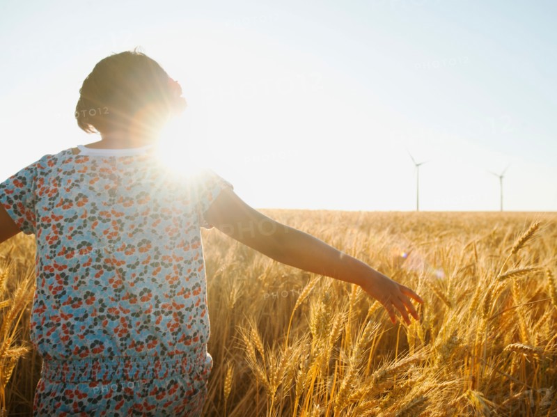 Girl (10-11) walking in glorious sunshine amidst wheat.
