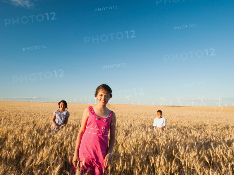 Girls (10-11, 12-13) and boy (8-9) standing in wheat field.