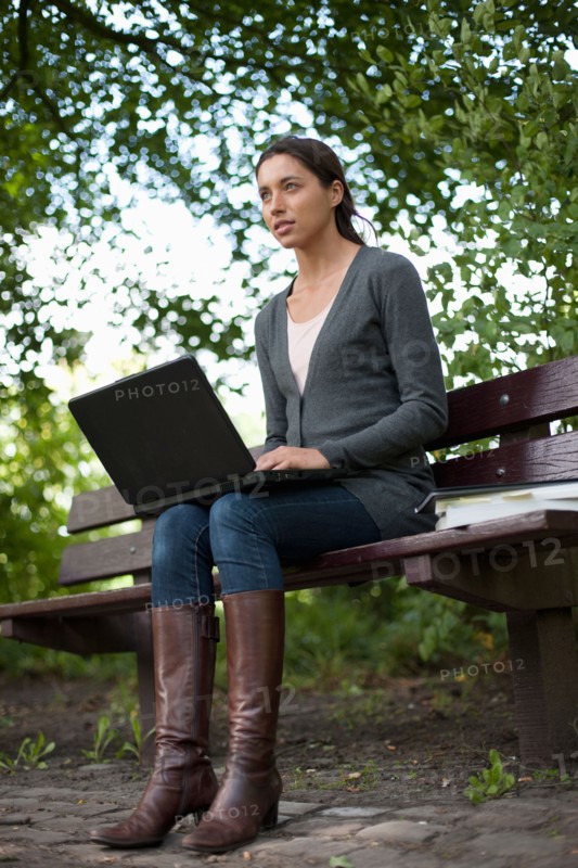 Young woman sitting on park bench using laptop. Photo : Jan Scherders