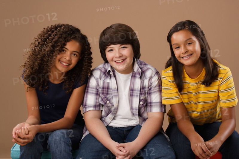 Studio portrait of boy and girls (10-11) sitting side by side. Photo : Rob Lewine