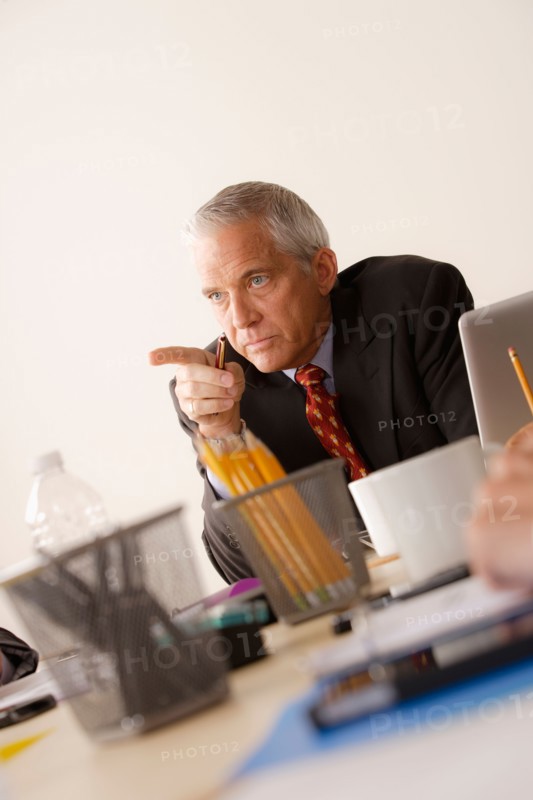 Businessman pointing finger from behind desk. Photo: Rob Lewine