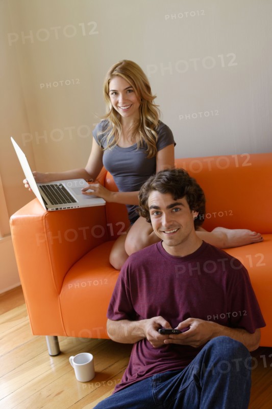 Young couple in living room, using phone and laptop. Photo : Rob Lewine