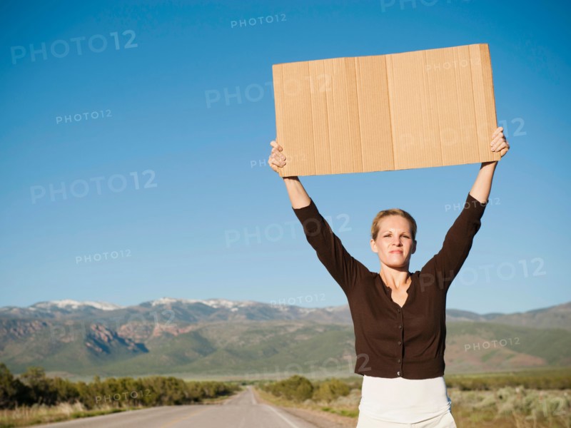 Mid-adult woman hitch-hiking in barren scenery. Photo: Erik Isakson