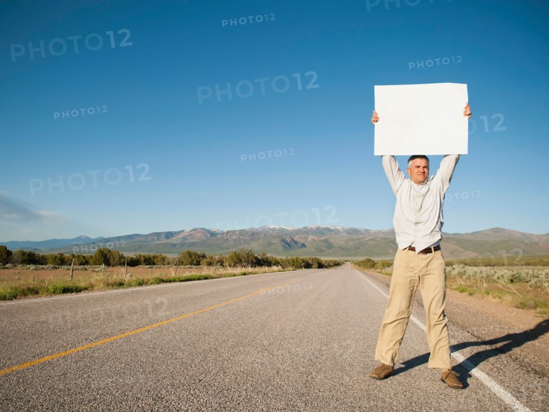 Mid-adult man hitch-hiking in barren scenery. Photo: Erik Isakson