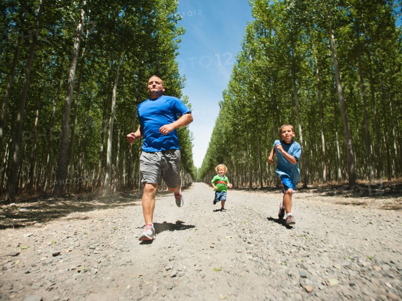 Father with sons (2-9) running down country road.