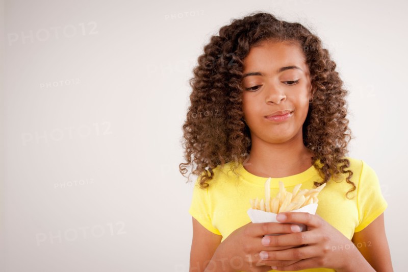 Studio portrait of girl (10-11) holding french fries. Photo : Rob Lewine