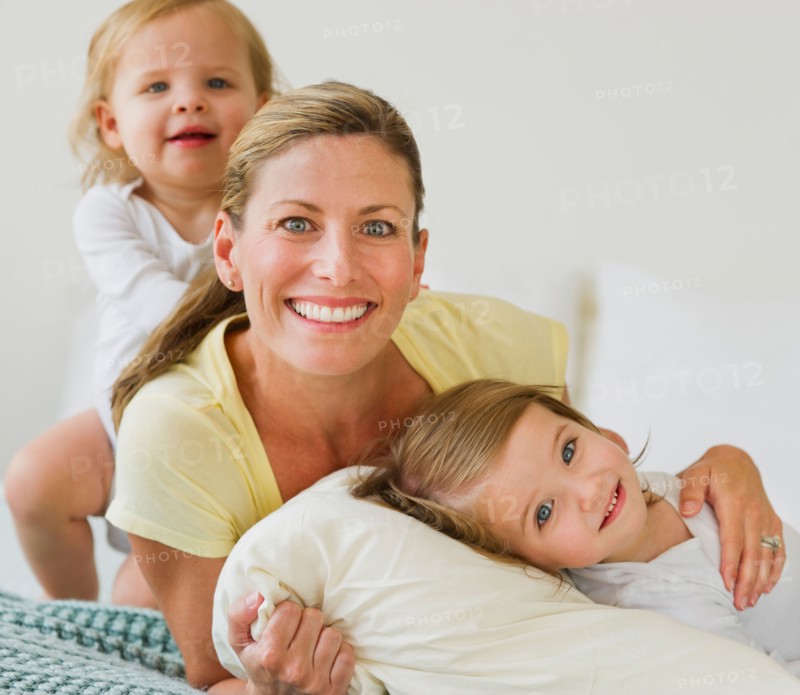 Portrait of mother with daughters (2-3) on bed.