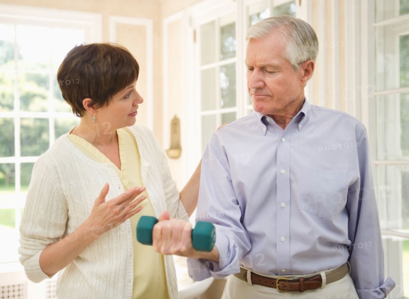 Senior man lifting dumbbell, nurse assisting him.