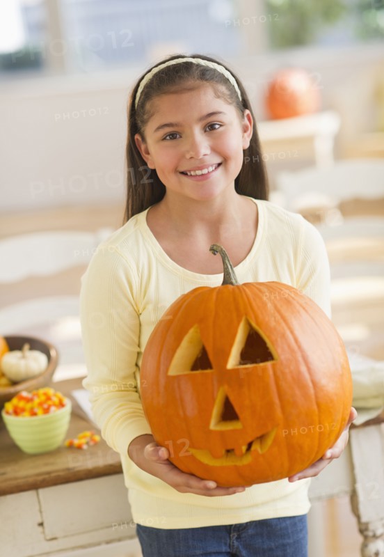 Portrait of girl (10-11) holding Jack o lantern.