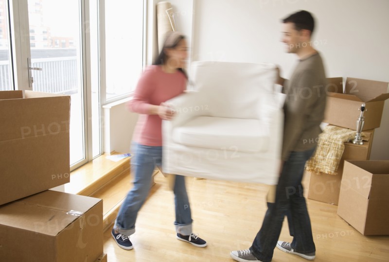 Man and woman carrying chair in new house.