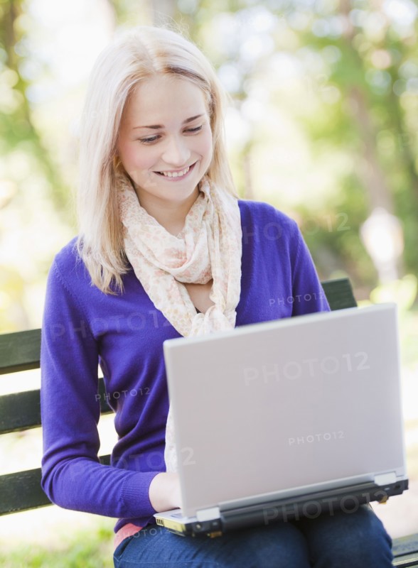 USA, New York, New York City, Manhattan, Central Park, Young woman sitting on bench and using laptop. Photo : Daniel Grill