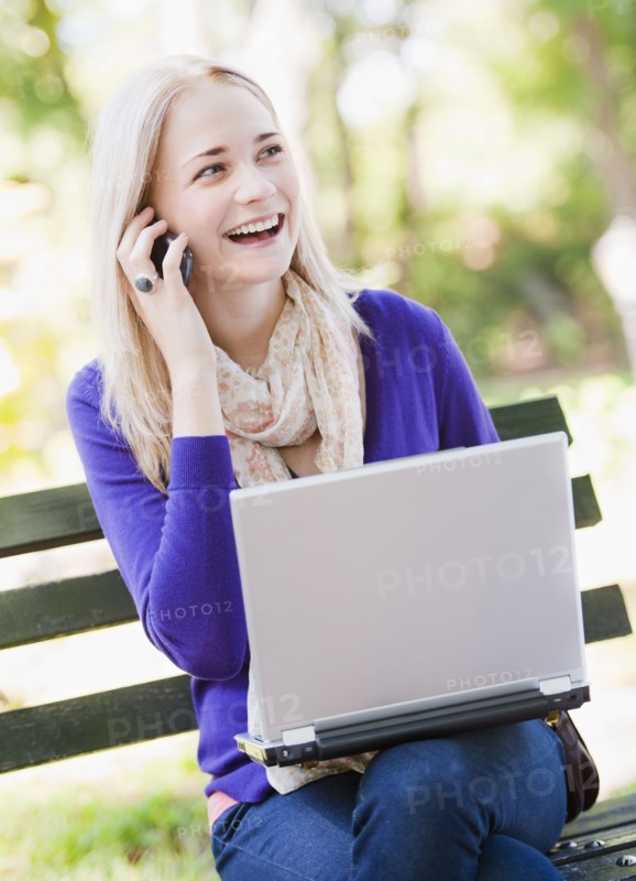 USA, New York, New York City, Manhattan, Central Park, Young woman sitting on bench with laptop and mobile phone. Photo : Daniel Grill