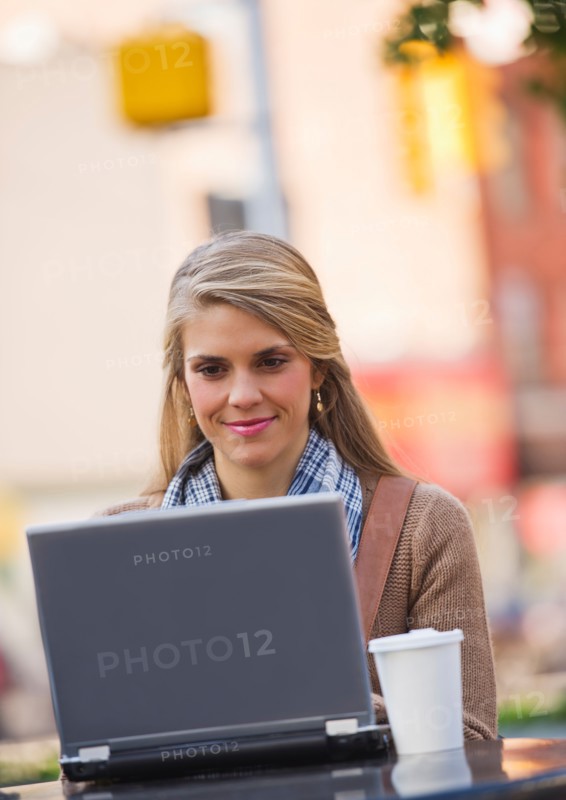 Young woman sitting with laptop in sidewalk cafe. Photo : Daniel Grill