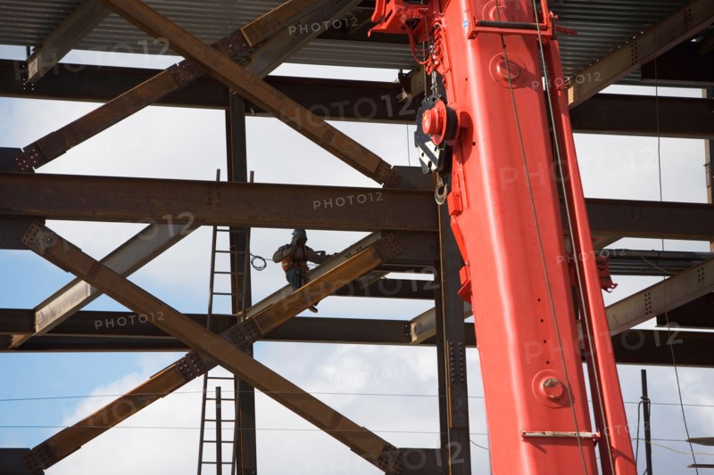 Construction worker working on unfinished structure, red crane in foreground. Photo : fotog