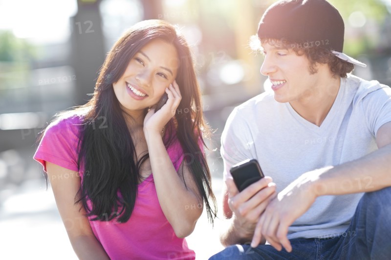 Young multi-racial couple sitting together playing with their mobile phones. Photo : Take A Pix Media