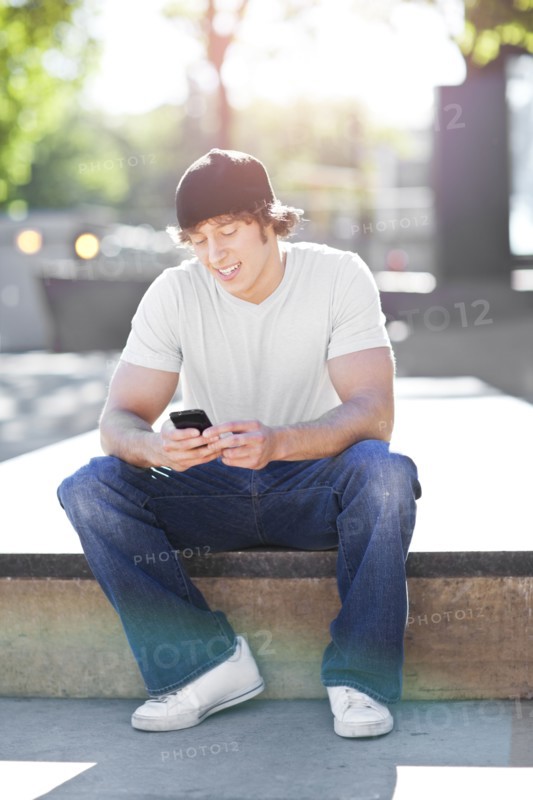 Young man sitting outdoors, text messaging. Photo : Take A Pix Media