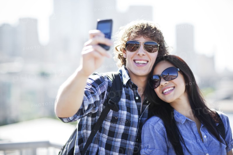 USA, Washington, Seattle, Couple wearing sunglasses photographing themselves with smart phone. Photo : Take A Pix Media
