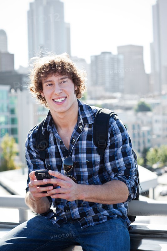 USA, Washington, Seattle, Man text messaging outdoors, skyline in background. Photo: Take A Pix Media