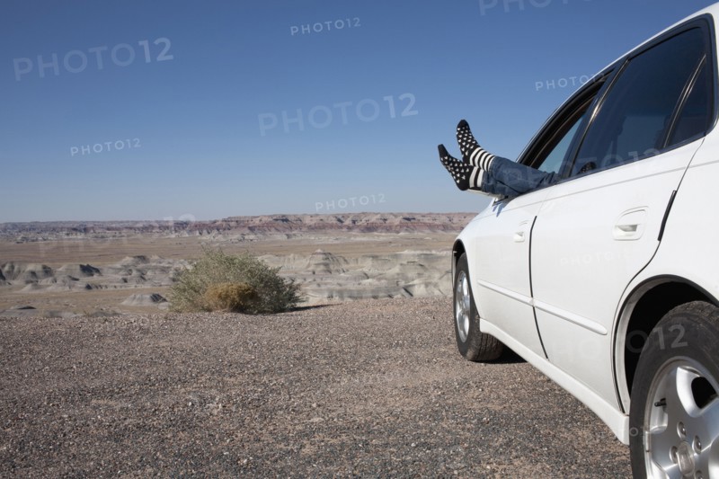 USA, Arizona, Winslow, Woman sticking feet out of car window parked in desert. Photo: Winslow Productions