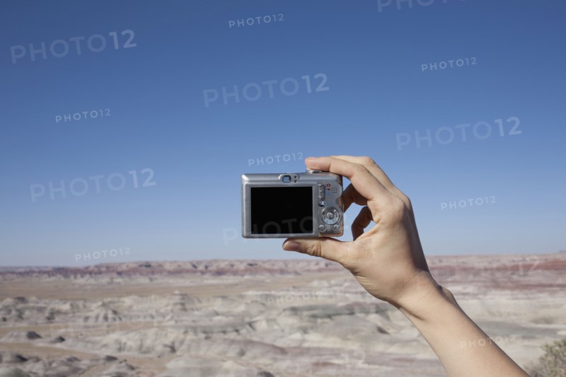 Hand of woman holding camera up against blue sky. Photo : Winslow Productions