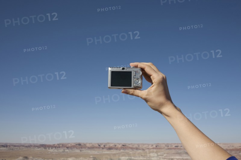 Hand of woman holding camera up against blue sky. Photo : Winslow Productions