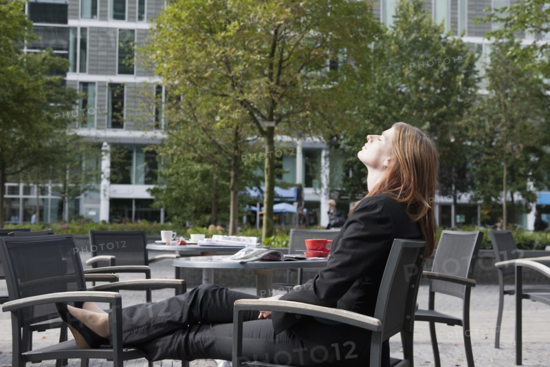 The Netherlands, Amsterdam, Businesswoman relaxing on chairs on sidewalk. Photo: Jan Scherders
