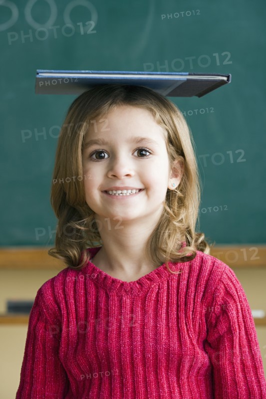Portrait of girl (6-7) balancing book on head. Photo: Rob Lewine
