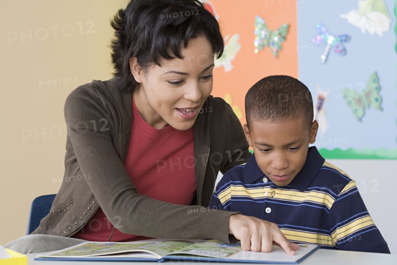 Teacher helping boy (6-7) in reading. Photo : Rob Lewine
