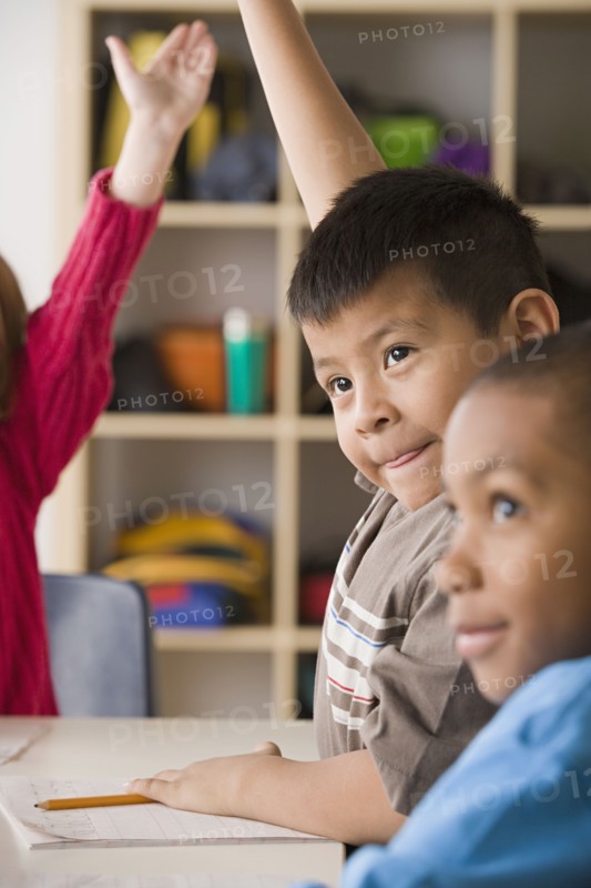Children (6-7) raising hands in classroom. Photo: Rob Lewine