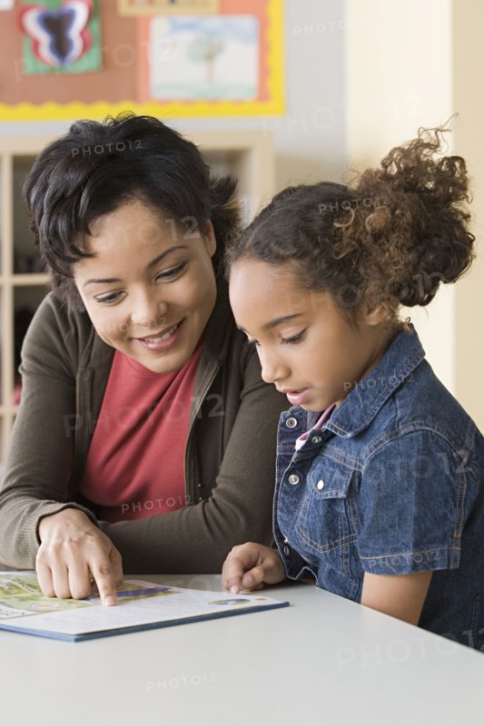 Teacher helping girl (6-7) to read. Photo : Rob Lewine