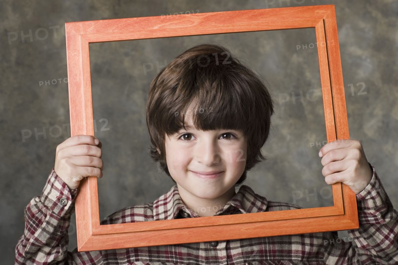Smiling boy (6-7) looking through frame, studio shot. Photo : Rob Lewine