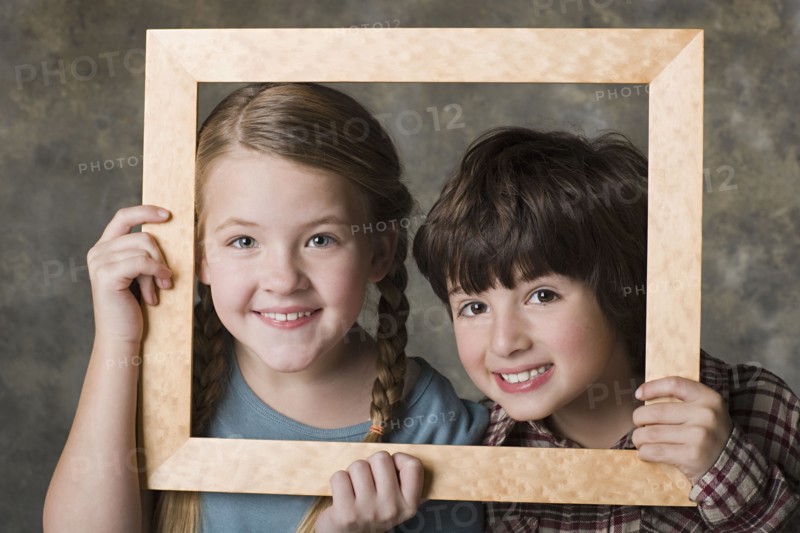 Portrait of girl (8-9) and boy (6-7) looking through frame, studio shot. Photo : Rob Lewine
