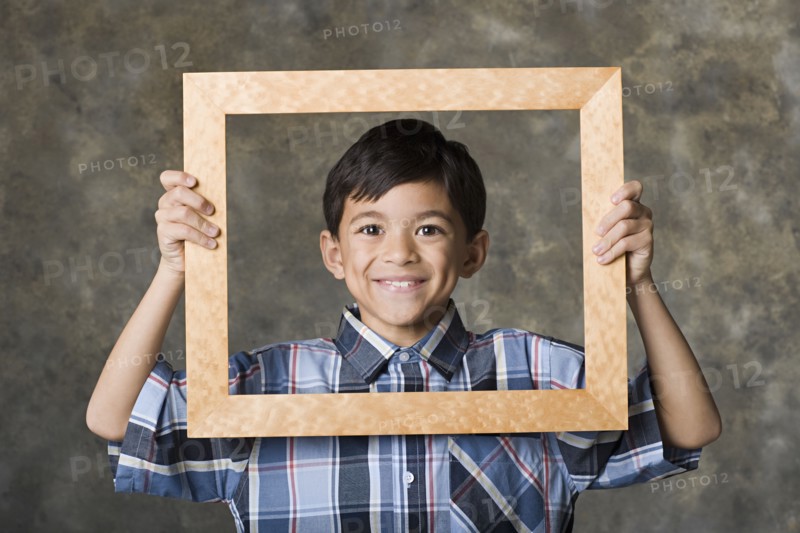 Portrait of smiling boy (8-9) looking through frame, studio shot. Photo : Rob Lewine