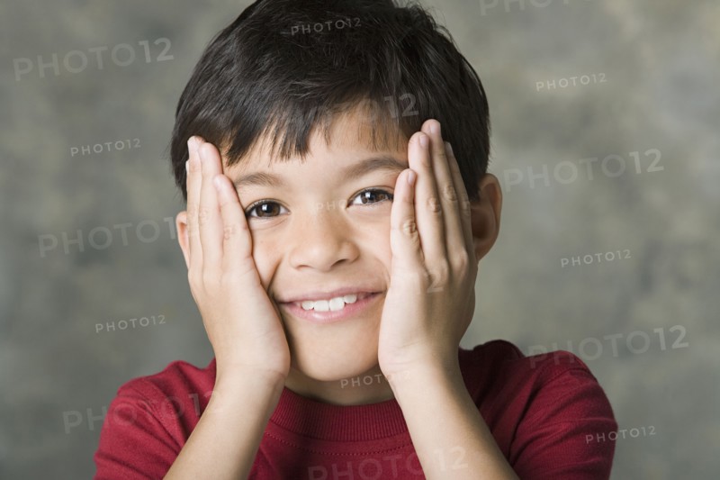 Portrait of smiling boy (8-9) with hands on face, studio shot. Photo : Rob Lewine