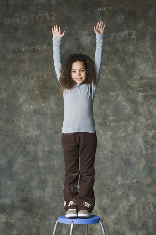 Portrait of smiling girl (8-9) with arms raised, studio shot. Photo : Rob Lewine