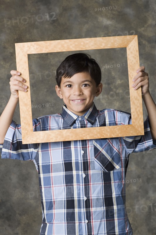 Portrait of smiling boy (8-9) looking through frame, studio shot. Photo : Rob Lewine