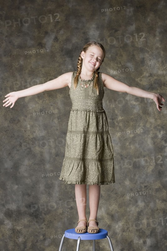 Portrait of smiling girl (8-9) standing on stool, studio shot. Photo : Rob Lewine