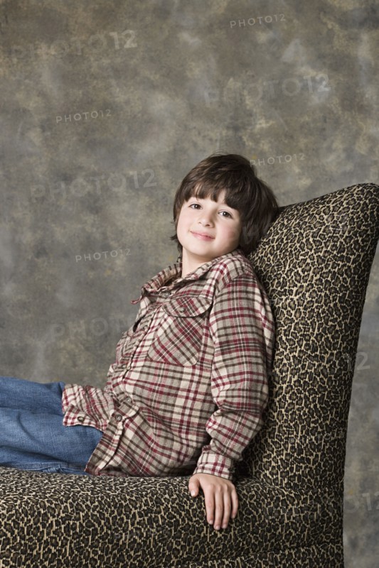 Portrait of boy (6-7) sitting on chair with animal print, studio shot. Photo : Rob Lewine
