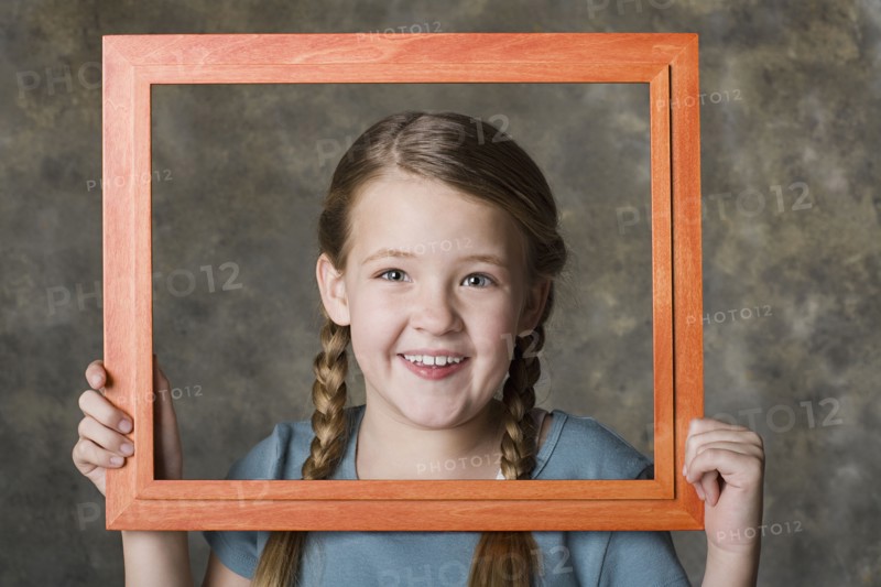 Portrait of smiling girl (8-9) holding frame, studio shot. Photo : Rob Lewine