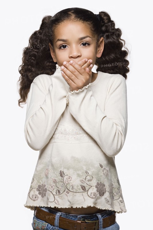 Studio portrait of girl (8-9) with pigtails covering mouth with hands. Photo: Rob Lewine