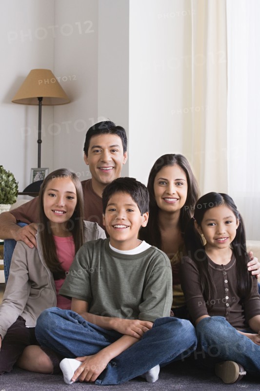 Portrait of happy family with three children (8-9, 10-11) sitting on floor. Photo: Rob Lewine