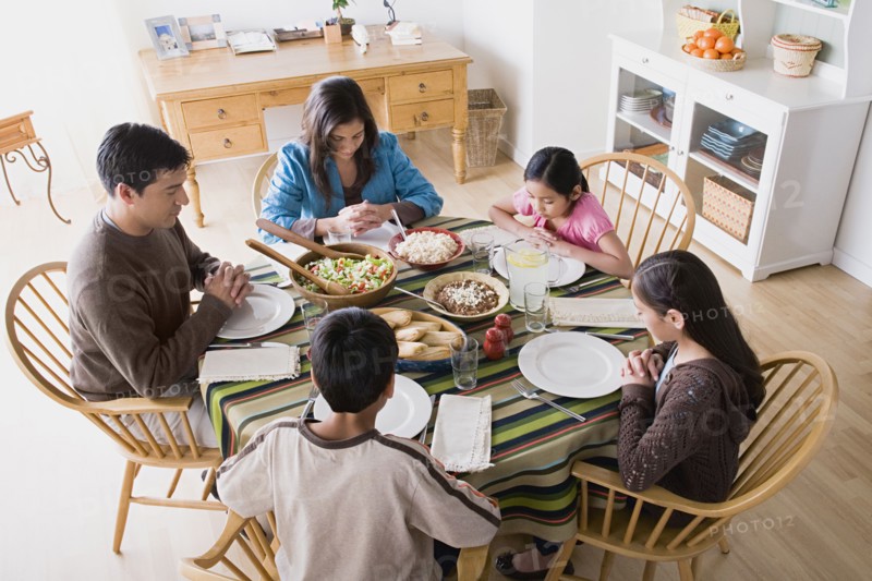 Family with three children (8-9, 10-11) praying at table before dining. Photo: Rob Lewine